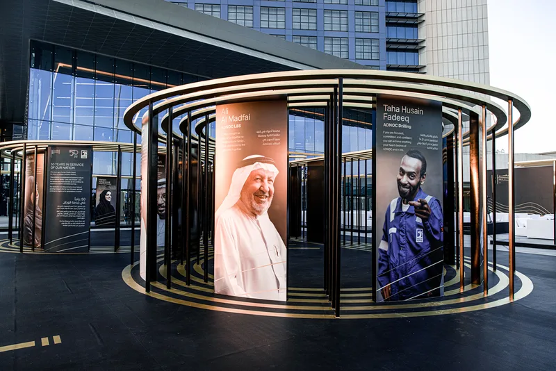 ADNOC 50 Faces gallery installation featuring reflective vinyl scenic finishes in Abu Dhabi.