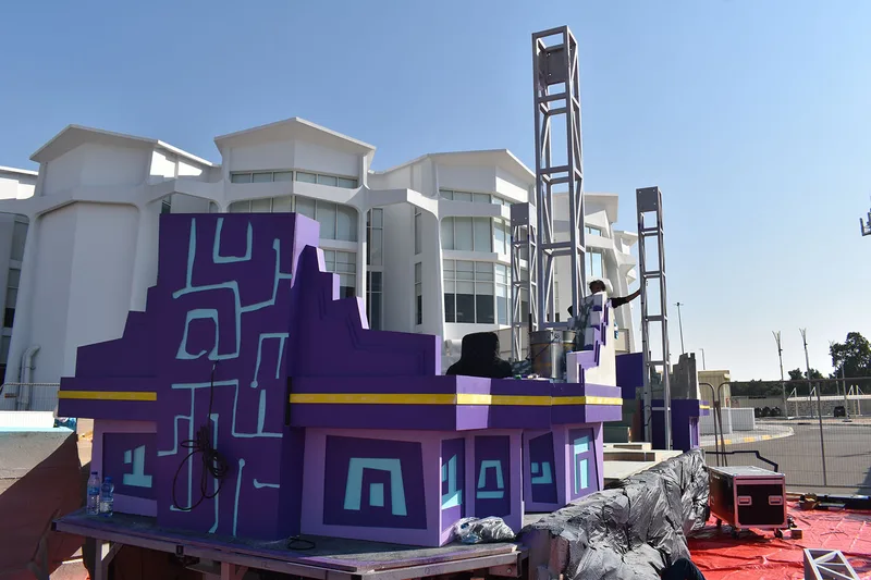 Purple scenic cladding wrapped around the truck base while tall support frames are assembled for the Mansour Festival float.