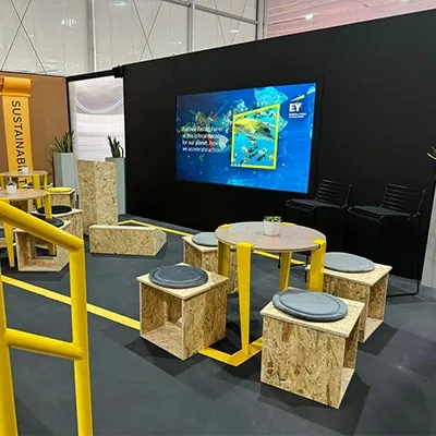 Custom OSB-style scenic furniture and yellow metal railings within the EY COP28 exhibition environment.