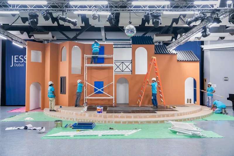 Evolution Scenic painters checking colour consistency beneath bright, even workshop production lighting