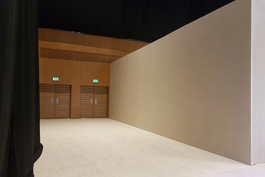 Solid scenic wall beside black drape where different site functions require different systems
