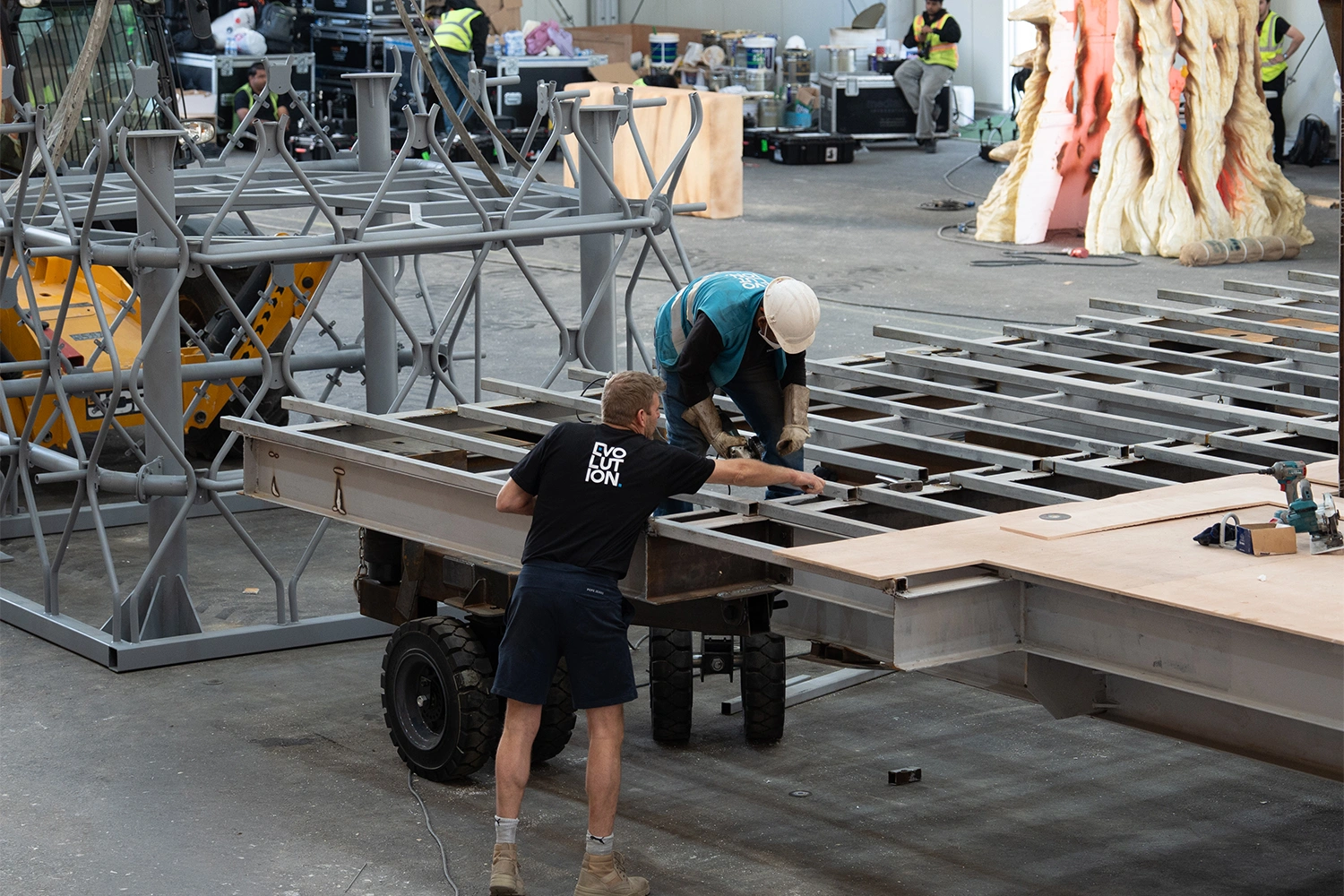 Fabricated scenic components laid out beside transport drawings and a site access plan in the workshop.
