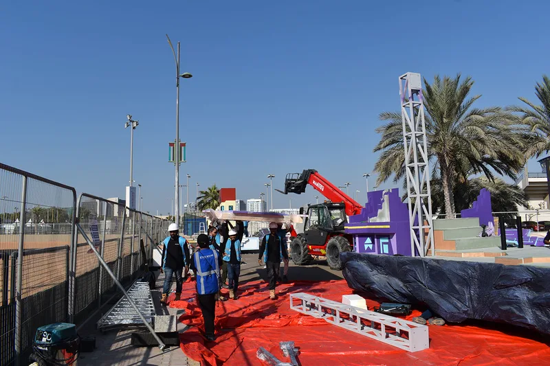 Crew using lifting equipment around the tall Mansour Festival float structure during on-site assembly.