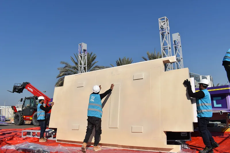 Crew positioning a large lightweight scenic panel during construction of the Mansour Festival parade float.