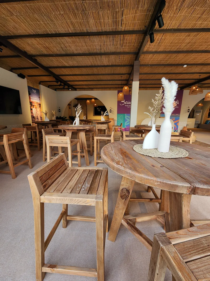 Natural solid-wood round tables arranged within the Visit Saudi main tent.