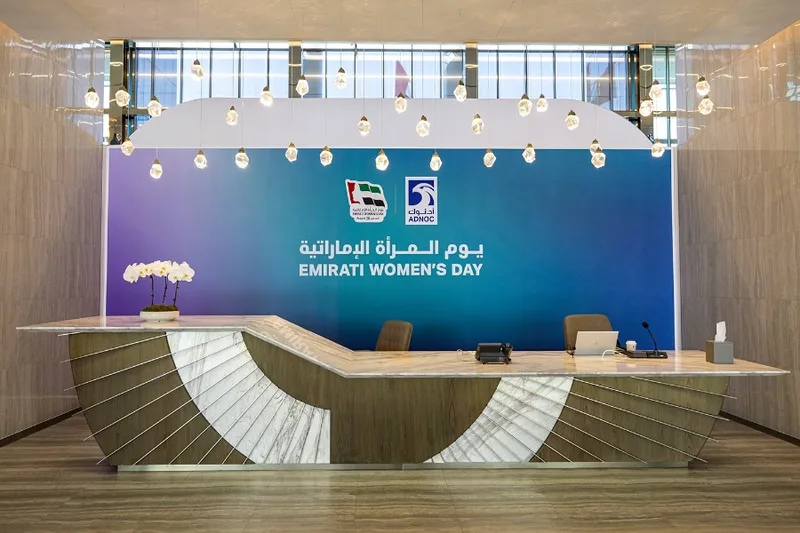 Curved reception counter positioned before the Emirati Women’s Day scenic wall.
