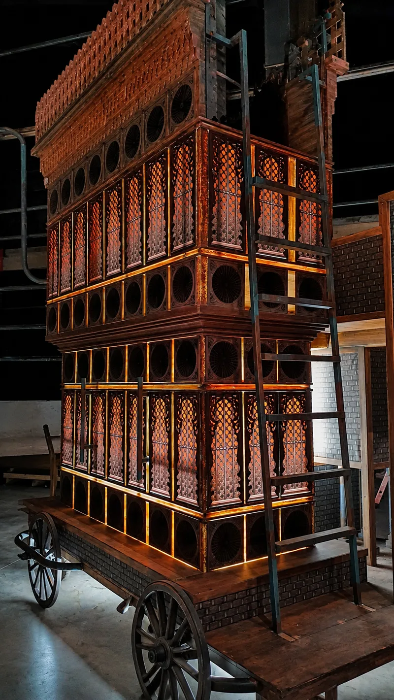 Illuminated Terhal scenic tower cart showing ornate wood detailing, glowing lattice panels and wheeled base during backstage setup in Riyadh.