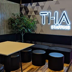 THA Stand seating lounge with illuminated branding, geometric scenic wall and integrated bench seating.
