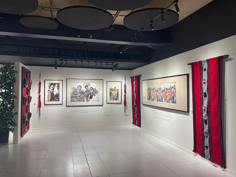 White modular exhibition partitions displaying framed cultural artwork and textile installations.