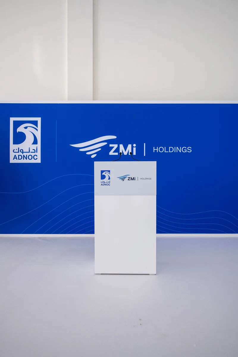 Custom white lectern positioned against the ADNOC and ZMI branded scenic wall.
